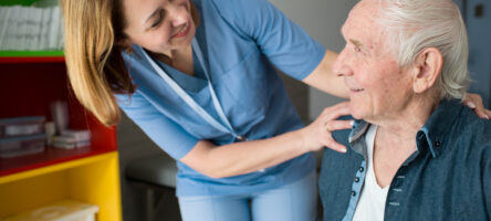 Happy Caretaker Assisting Senior Man. Friendly Nurse Supporting Old Man With Parkinson's Disease