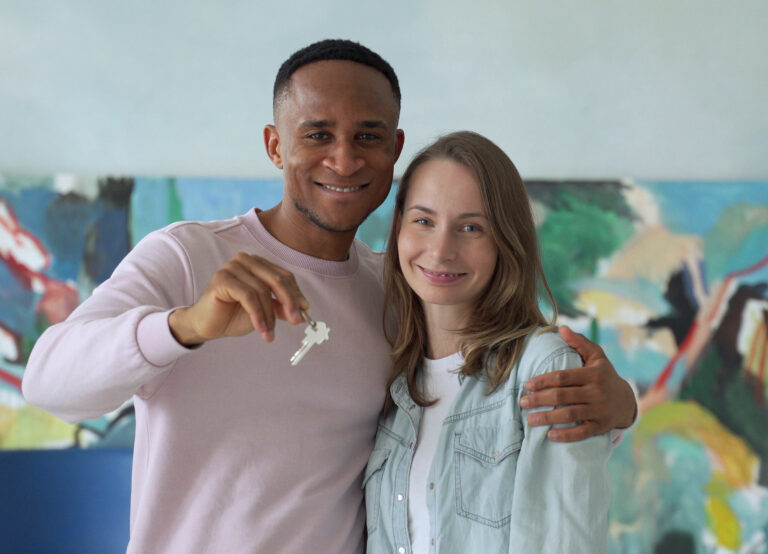 Cheerful Young Couple Holding Keys And Smiling While Standing In Their New House